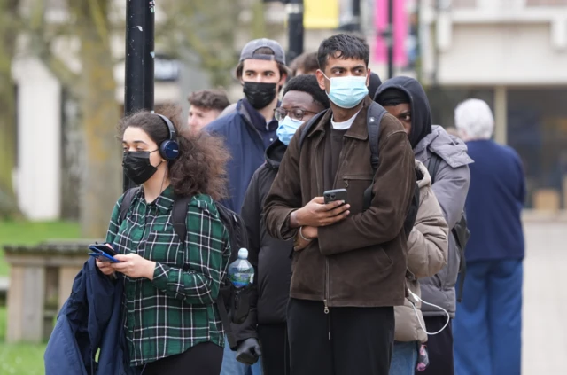 Students wearing face masks queue outside a university building to collect antibiotics