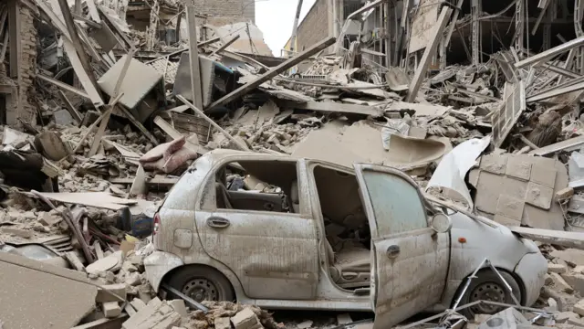 A damaged vehicle at a strike site in Tehran, there is grey rubble everywhere