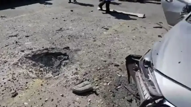 A hole in the tarmac and a damaged car seen at the site of reported missile impact in Tel Aviv