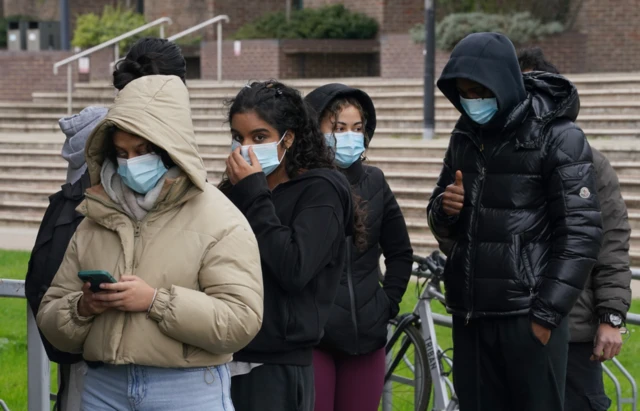 Students wearing face masks queue outside a university building to collect antibiotics