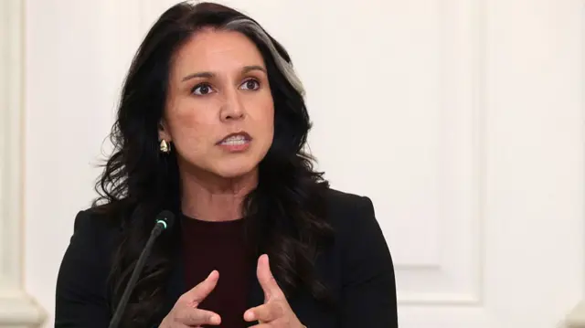 Gabbard sits in front of a microphone wearing a maroon shirt and black jacket