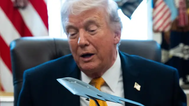 Trump speaks while looking at a miniature model stealth bomber in front of him in the Oval Office.