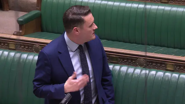 Health Secretary Wes Streeting turning behind him to speak to MPs on the green benches in the House of Commons. He is wearing a dark blue suit