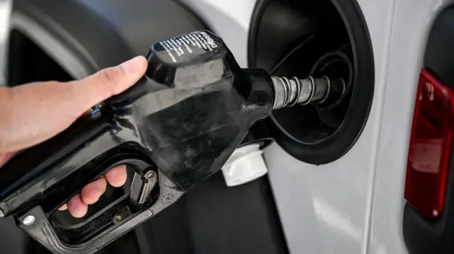 A man uses a black gas pump at a petrol station