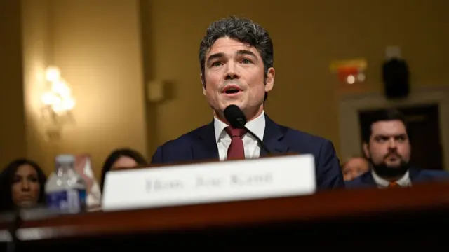 Joe Kent sits at a desk and speaks into a microphone