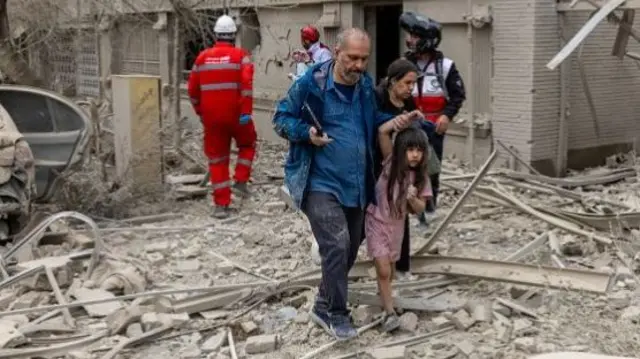 People make their way through debris following a strike on a residential building on March 16, 2026 in central Tehran, Iran.