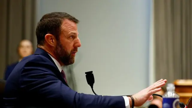 Markwayne Mullin in a dark suit with his arm extended out in front of him as he speaks into a microphone.