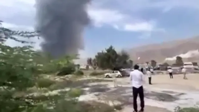 A man watches on in the distance as thick black acrid smoke billows into the air