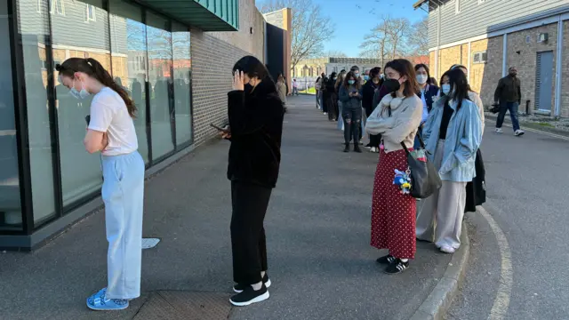 Queue of people on road outside building