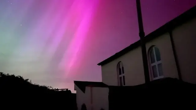 Aurora Borealis with pink and purple hues above a building.