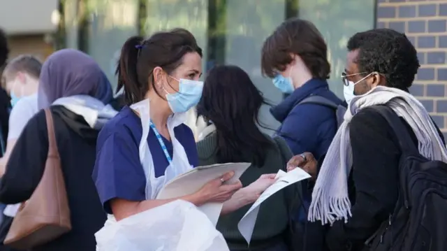 A nurse hands out information sheets to those standing in line
