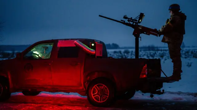 A soldier on the back of a pick-up truck with a gun.