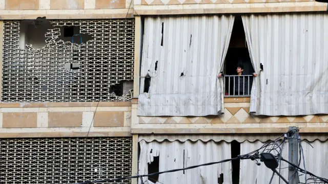 A person looks out of a balcony in the aftermath of an Israeli strike in Bierut's Zuqaq al-Blat district