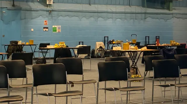 Chairs laid out in sports hall with tables in the background
