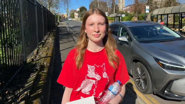 A girl stands in a street holding a water bottle