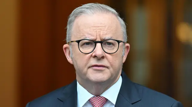 Australia's Prime Minister Anthony Albanese speaking in a navy suit and red and white chequered tie.