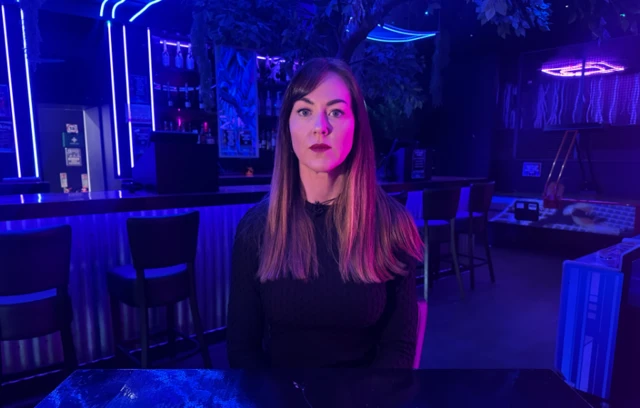 Louise Jones-Robert sits at a table on her nightclub, which has been lit up by neon blue lighting