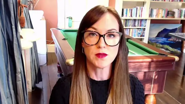 Louise Jones-Roberts speaks into a webcam in front of a pool table and a bookcase