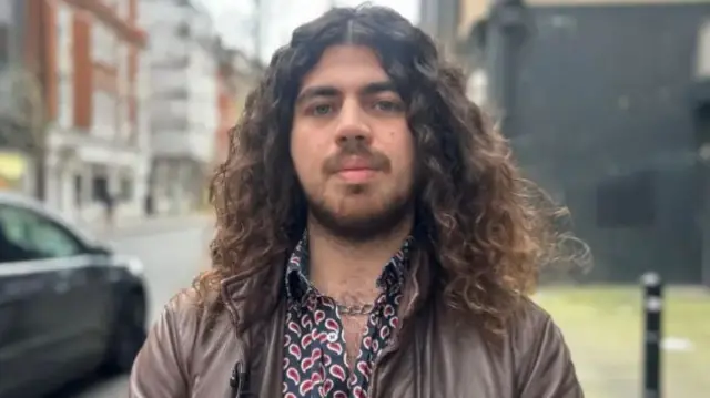 Theo dal Pozzo stands outside in a patterned shirt and leather jacket.