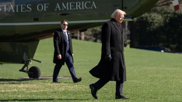 Trump walking along with Marine Force One helicopter in the background, and a secret service agent.