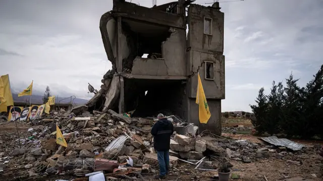 a destroyed house surrounded by rubble, where a man stands