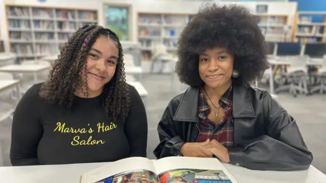 From left: Mya and Sahara sit at a table with a book open in front of them.