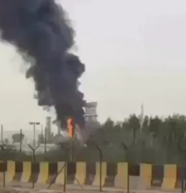 A screenshot from a video showing a fire and cloud of smoke rising over an oil refinery