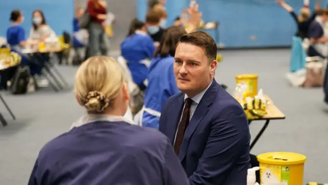 Wes Streeting speaks to a medical worker during a visit to the University of Kent campus in Canterbury. A number of workers can be seen at desks spread out in a hall behind Streeting