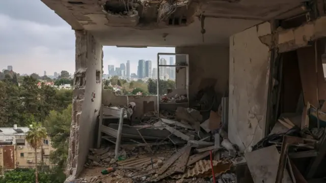 a destroyed room in an apartment building, with walls blasted out, looking out over trees and skyline