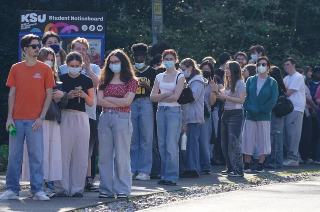 Group of young people queuing outside in the sun wearing face masks on University of Kent's Canterbury campus