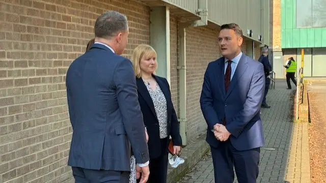 Wes Streeting wearing suit speaking to three people outside building