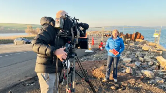 Victoria Graham stood in front of a camera by the fallen sea wall.