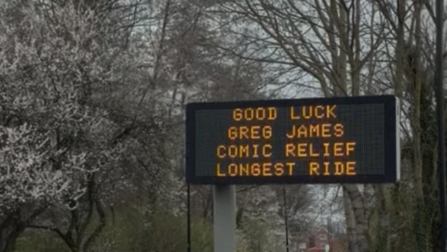 An electronic road sign displays the message: "GOOD LUCK GREG JAMES COMIC RELIEF LONGEST RIDE"