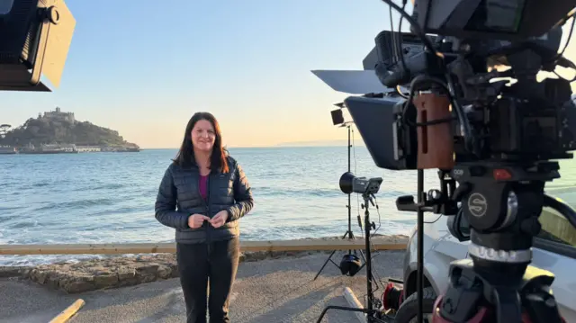 Tamsin Melville stood in front of a camera with St Michael's Mount in the distance.