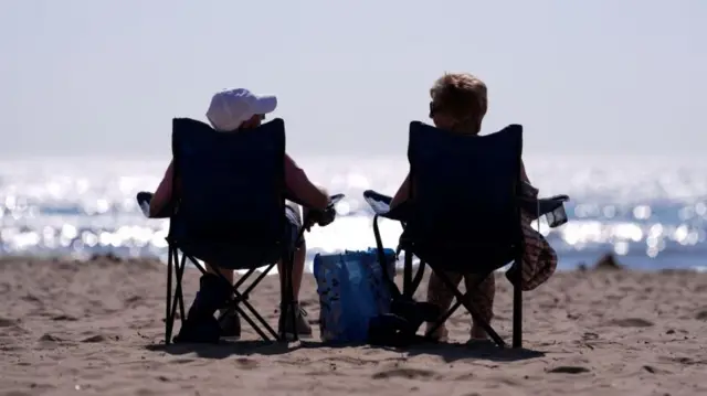 Two people sat in fold-out camping chairs on a sandy beach