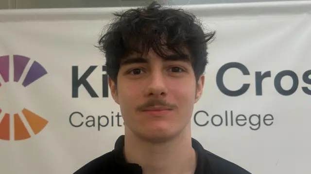 Rio Ndou in a black top. He has dark hair and a moustache.