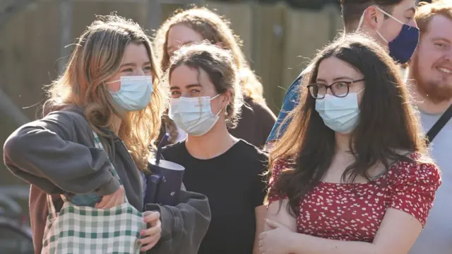 A group of girls wear face masks as they wait in a queue