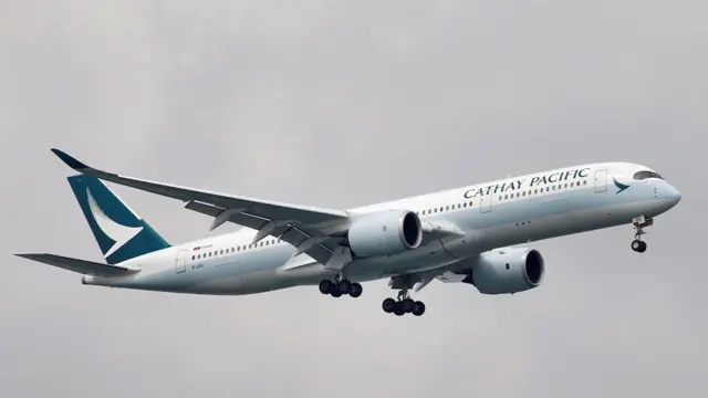 A Cathay Pacific Airways Airbus A350-900 aeroplane approaches to land, with a pale blue stripe painted across the body.