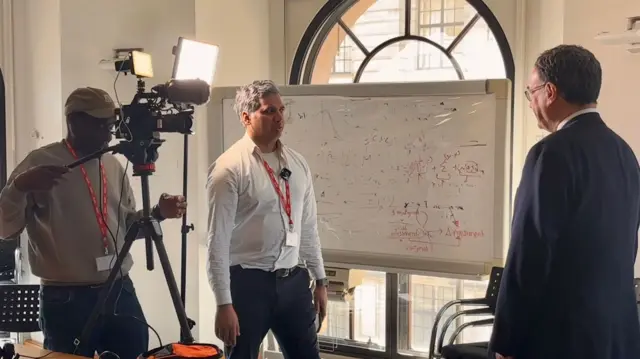 Media crew, including the BBC's Faisal Islam (C) interviews BoE governor Andrew Bailery (R) in a room inside the bank's building