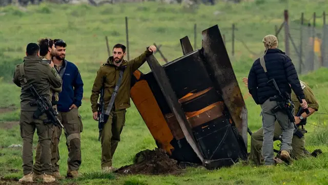 security officers standing beside large rocket, as tall as them, in a field of grass