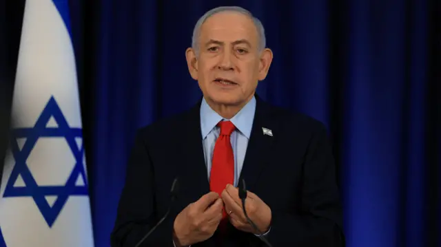 Netanyahu stands in front of an Israeli flag