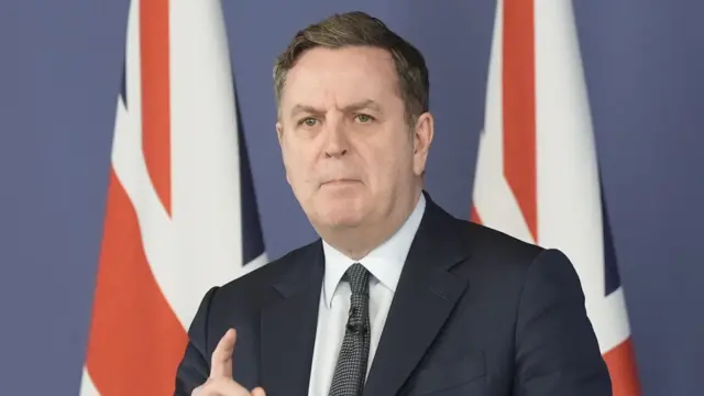 Shadow chancellor Mel Stride mid-speech, two UK flags behind him