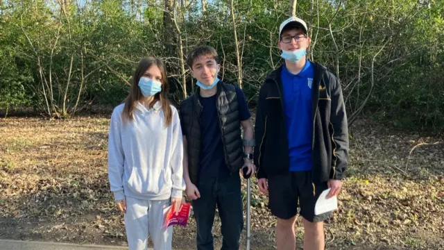 Three students stand on a path next to a woody area after receiving their vaccine