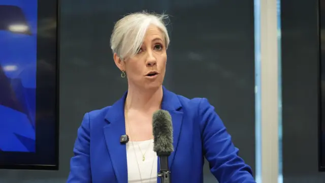 Lib Dems treasury spokesperson Daisy Cooper (woman in her 40s with short cropped grey hair) speaks on stage, wearing a blue blazer and white shirt