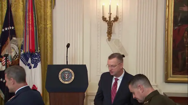 Three men standing in front of a stage on which is a wooden lectern with the US President sigil on