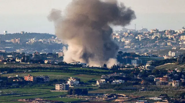 Smoke rising from a town with buildings and patches of green grass
