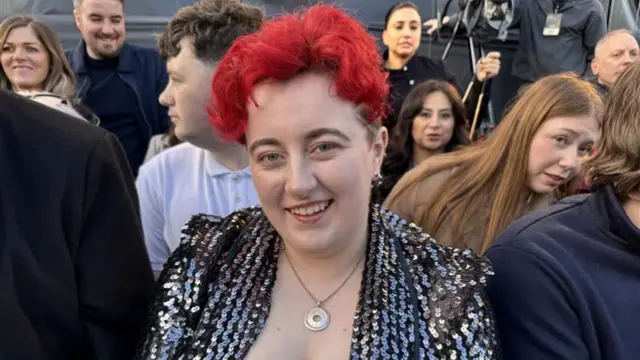 A woman with short curly bright red hair and a black sequin jacket