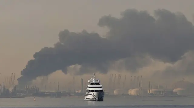 A yacht sails past a plume of smoke rising from the port of Jebel Ali following a reported Iranian strike in Dubai on March 1, 2026.