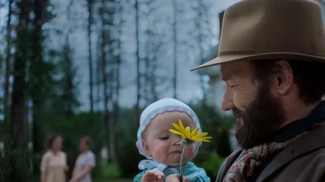 Train Dreams forest scene - Joel Edgerton with his on-screen baby daughter, he is showing her a yellow flower