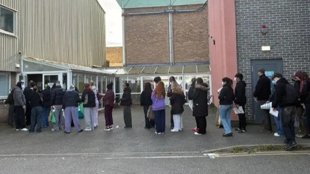 A queue of young people standing in a line outside a building.